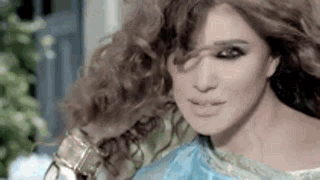 a close up of a woman 's face with her hair blowing in the wind and wearing a blue dress .