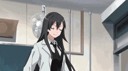 a girl in a white coat and tie stands in a room with a fan hanging from the ceiling
