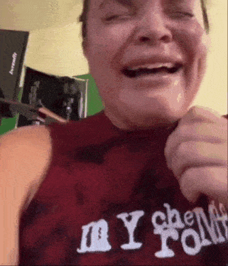 a woman wearing a red shirt with the word my on it is holding a pair of scissors to her mouth .