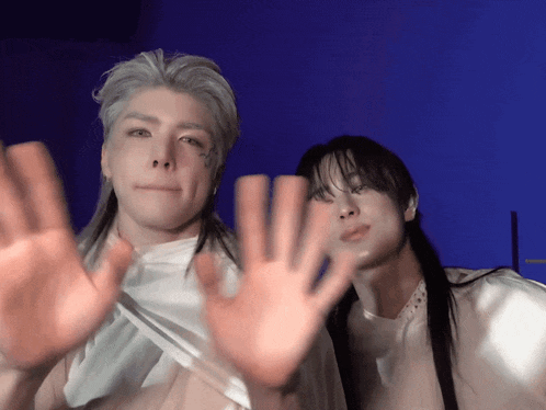 a man with long hair and a tattoo on his face stands next to another man with their hands up