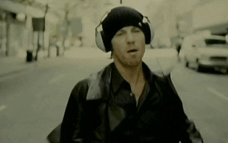 a man wearing headphones and a hat is walking down a city street .
