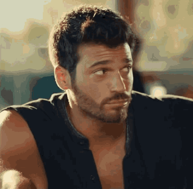 a man with a beard wearing a black tank top looks to the side
