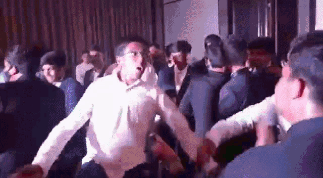 a man in a white shirt is dancing in a crowd of people in a room .
