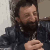 a man with a beard is sitting at a table holding a glass of beer .