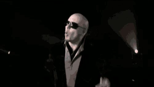 a bald man wearing sunglasses is standing in a dark room .
