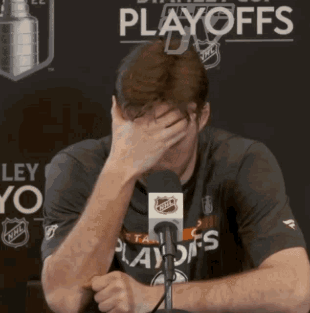 a man covering his face with his hand in front of a playoffs banner