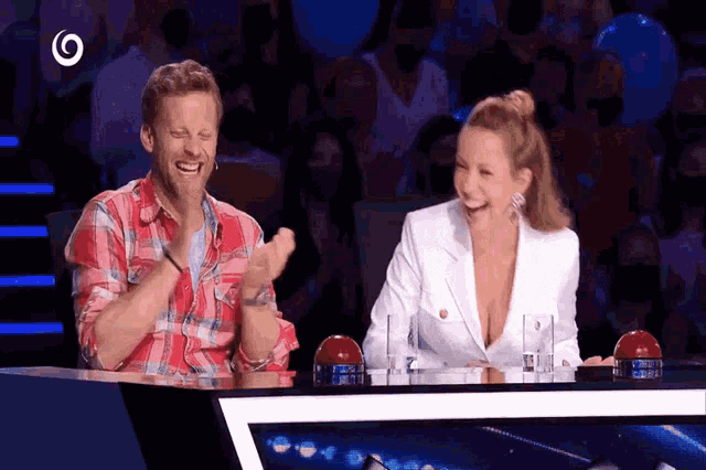 a man and a woman sit at a table laughing and clapping