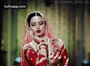 a woman in a red and gold dress and veil is looking down .