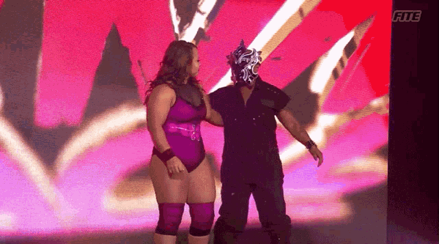 a woman in a purple bathing suit stands next to a man in a mask with the word fite on the bottom