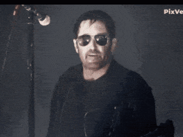 a man wearing sunglasses and a black jacket is smiling in front of a microphone with pixver written in the corner