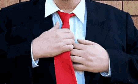 a man in a suit and tie is adjusting his red tie