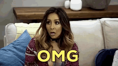 a woman is sitting on a couch with a surprised look on her face and the word omg written on her face .