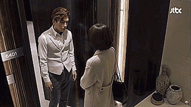 a man and a woman are standing in front of a door that says 6401