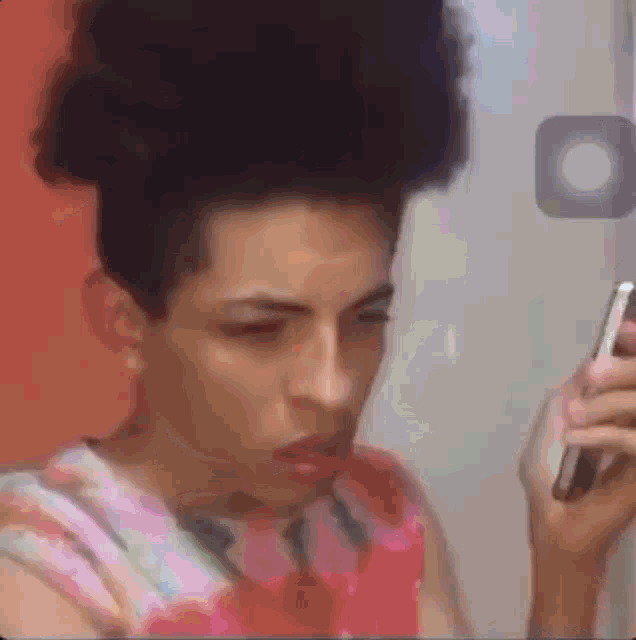 a man with a bun is looking at his cell phone in front of a mirror .