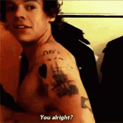 a shirtless man with a tattoo on his arm is asking if he is alright .