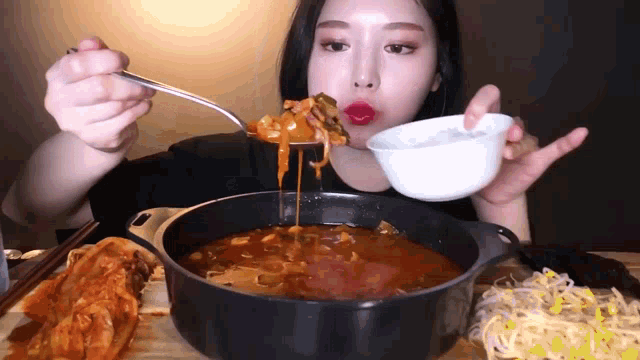 a woman is eating a pot of food with a spoon in her mouth