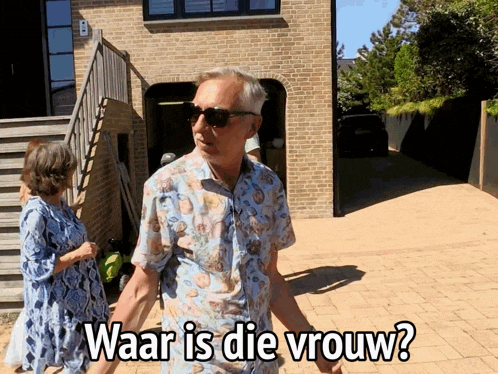 a man and woman are standing in front of a brick building and the man is wearing sunglasses and the woman is wearing a blue dress