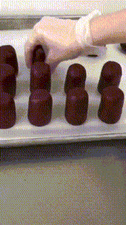 a person wearing gloves is reaching for a chocolate on a tray