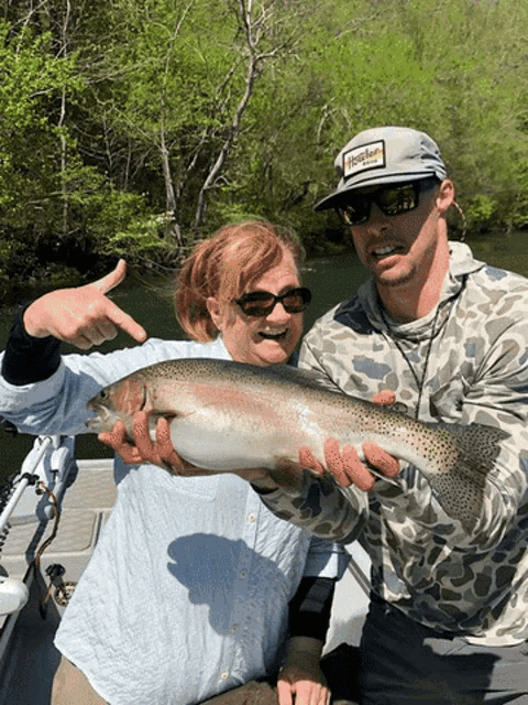 a man wearing a hat that says hooker on it holds a large fish