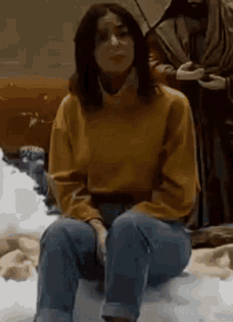 a woman in a yellow sweater and jeans is sitting on a pile of foam .