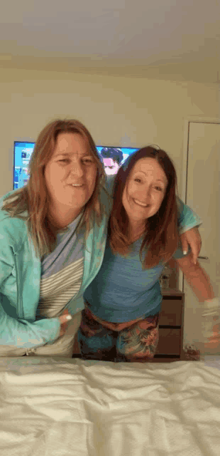 two women are posing for a picture on a bed