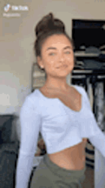 a woman wearing a white crop top and green shorts is standing in a living room .