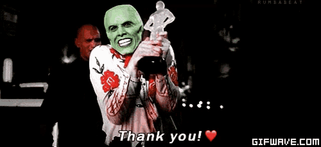 a man with a mask on his face is holding a trophy and says thank you .