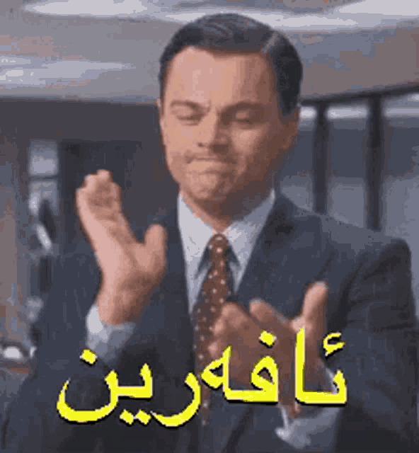 a man in a suit and tie is clapping his hands with arabic writing .