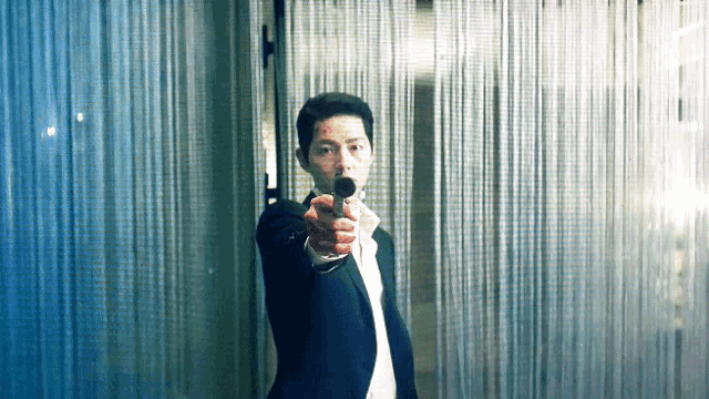 a man in a suit pointing a gun at the camera .