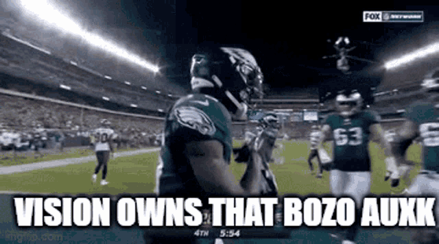 a football player is standing on a field with the words `` vision owns that bozo auxk '' .