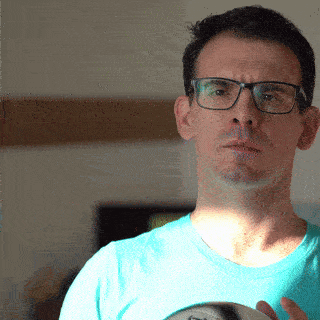 a man wearing glasses and a blue shirt is holding a ball