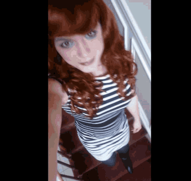a woman with red hair is standing on stairs wearing a striped shirt