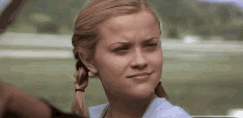 a woman with pigtails is making a funny face while sitting in the back seat of a car .