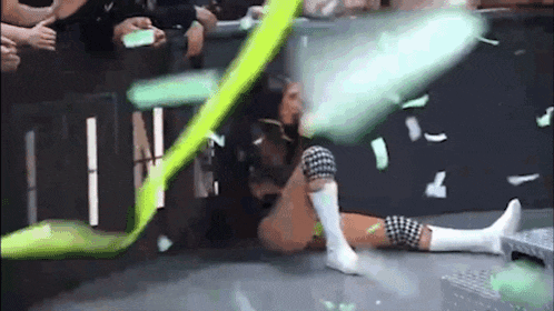 a woman is laying on the floor in a wrestling ring with a green ribbon flying around her .