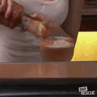 a woman is pouring hot sauce into a glass with a bar rescue sticker