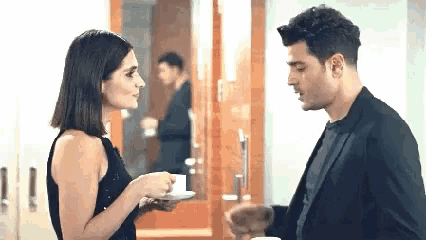a man and a woman are standing next to each other holding cups of coffee and looking at each other .