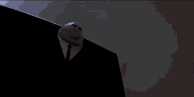 a man in a suit and tie is standing in the dark and pointing at the camera .