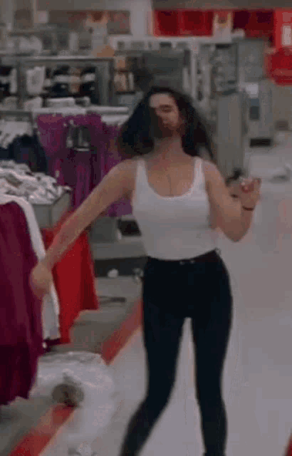 a woman is dancing in a store while wearing a white tank top and black pants .