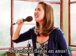 a woman singing into a microphone with the words our school flag is an anus below her