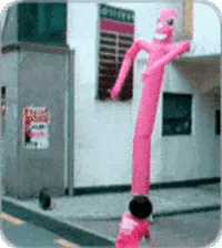 a pink air dancer is in front of a building with a sign on the wall that says ' a ' on it