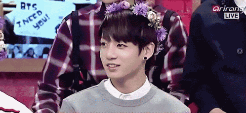 a boy with a flower crown on his head is sitting in front of a sign that says i need you