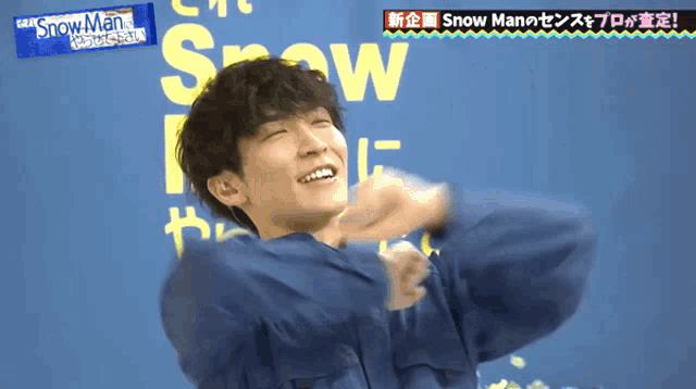 a man in a blue jacket is smiling in front of a sign that says snow man