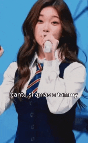 a girl in a school uniform is singing into a microphone while wearing a tie and vest .