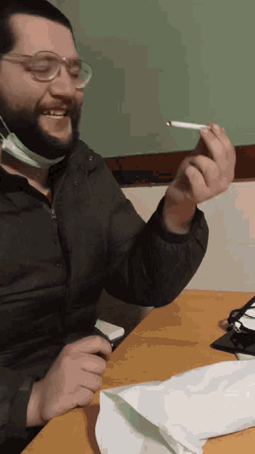 a man wearing glasses and a mask holds a cigarette in his right hand