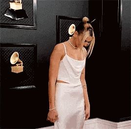 a woman in a white dress is standing in front of a wall with trophies .