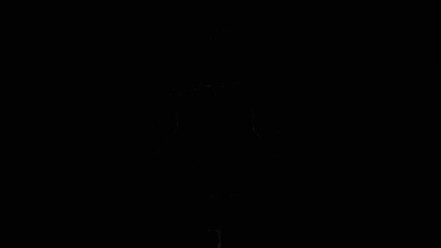 a man wearing a black shirt with yellow stripes on the sleeves is standing with his arms outstretched