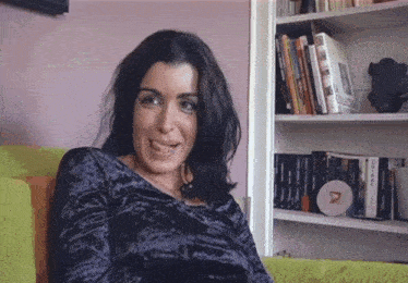 a woman is sitting on a couch in front of a bookshelf with the letter r on it .