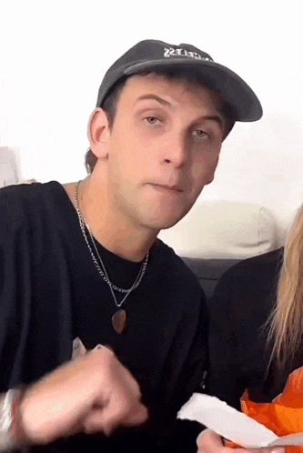 a young man wearing a hat and a necklace is eating chips