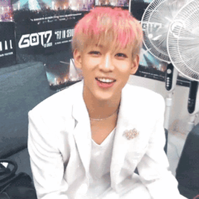 a boy with pink hair is smiling in front of a got7 poster