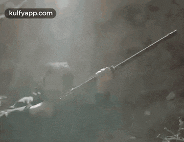 a black and white photo of a person holding a sword in the fog .